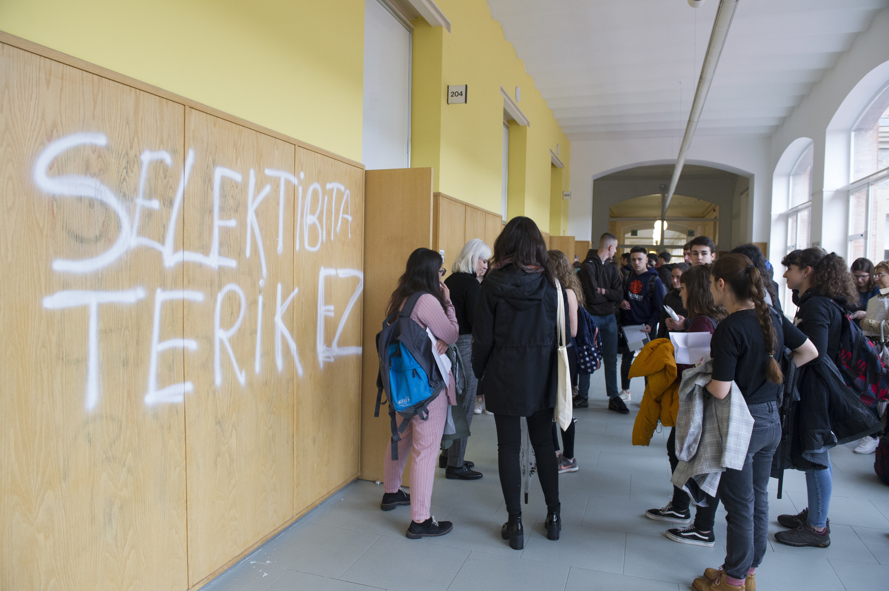 Varios alumnos esperan ser nombrados para acceder a una clase en el Aulario de Las Nieves en Vitoria junto a una pintada en contra de la selectividad.