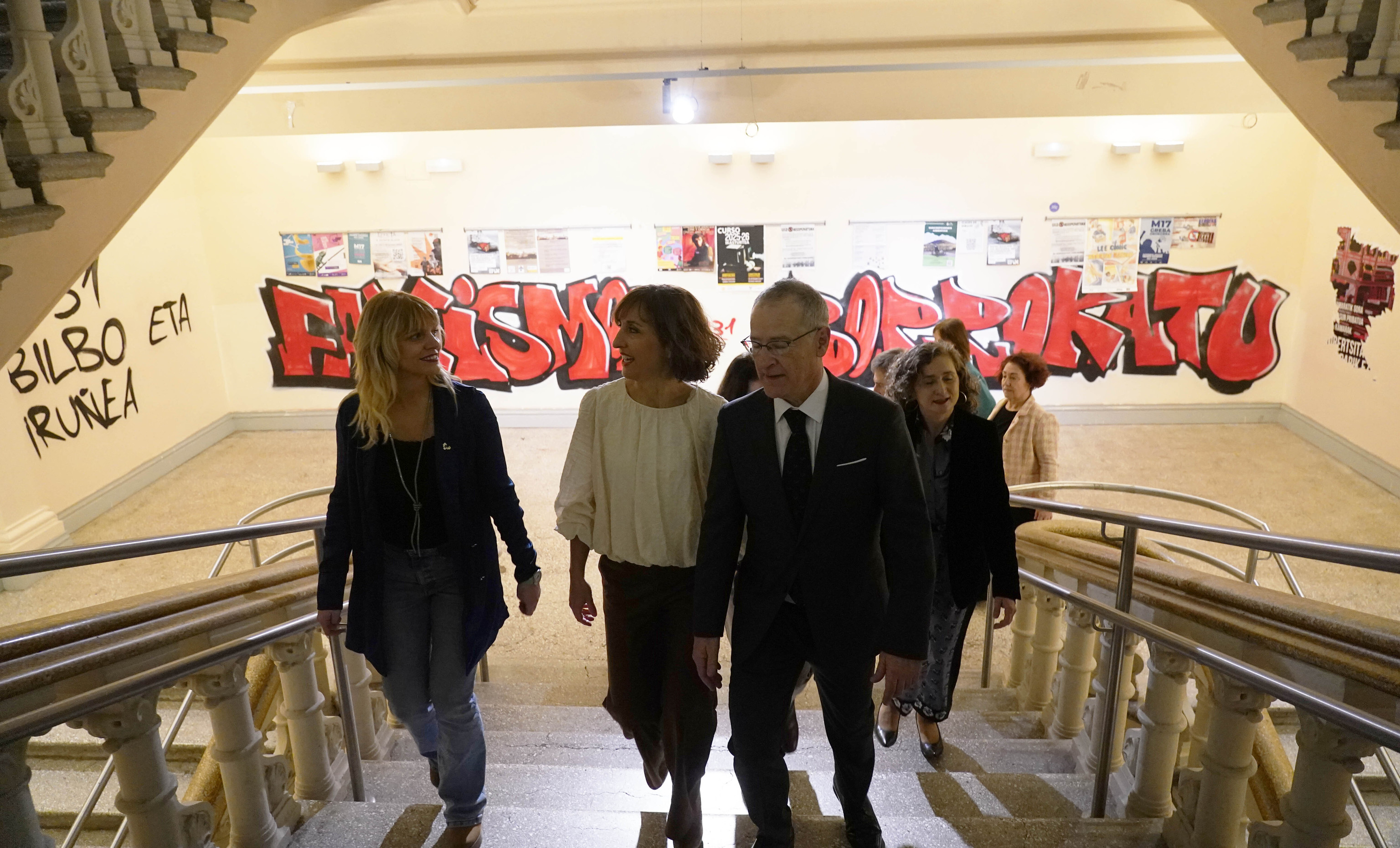 El rector Bengoetxea sube por las escaleras junto a su equipo en el Aulario de las Nieves con murales de colectivos radicales.