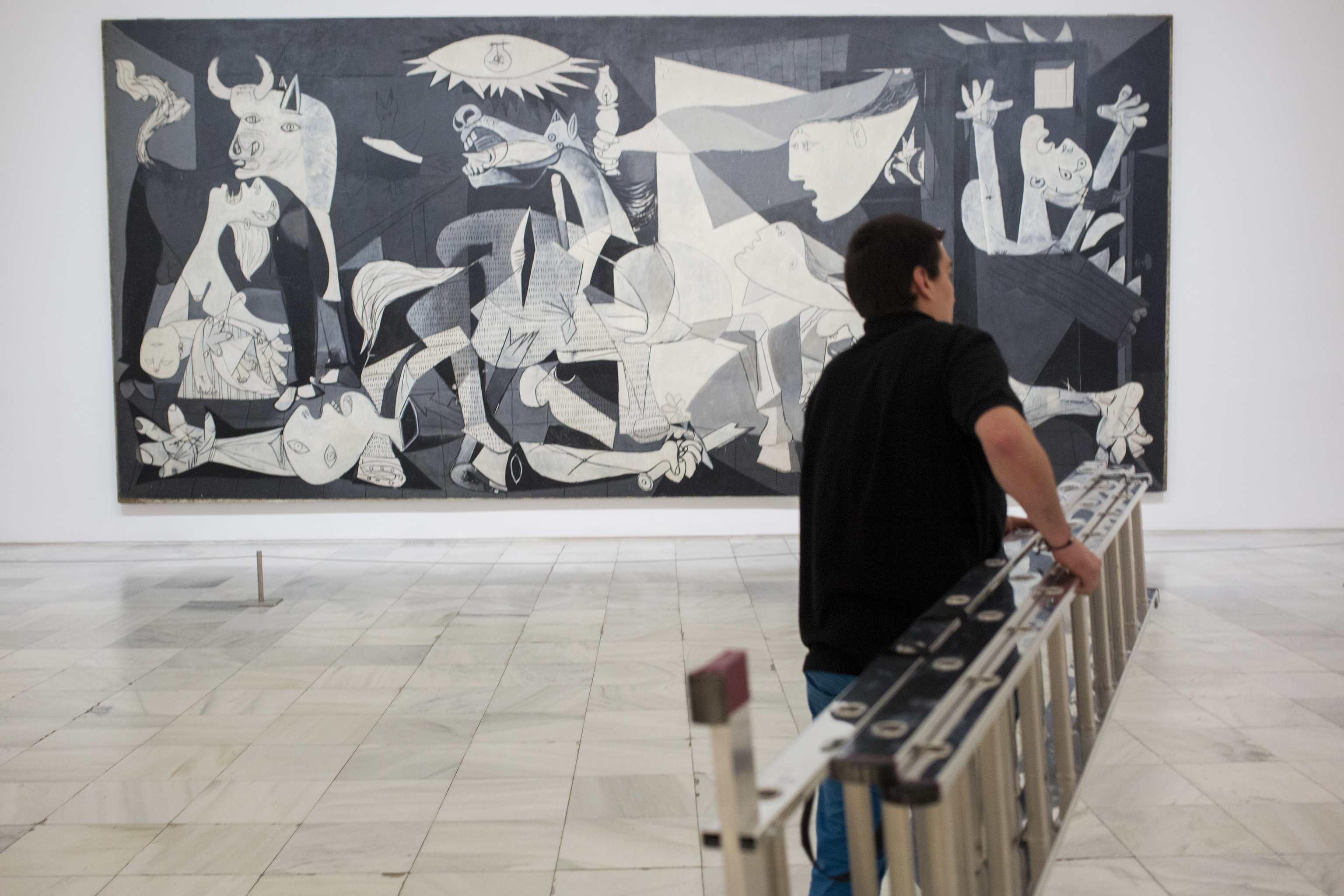 Un trabajador del museo Reina Sofía traslada una escalera en la sala en la que se encuentra expuesto el 'Guernica' de Pablo Picasso.