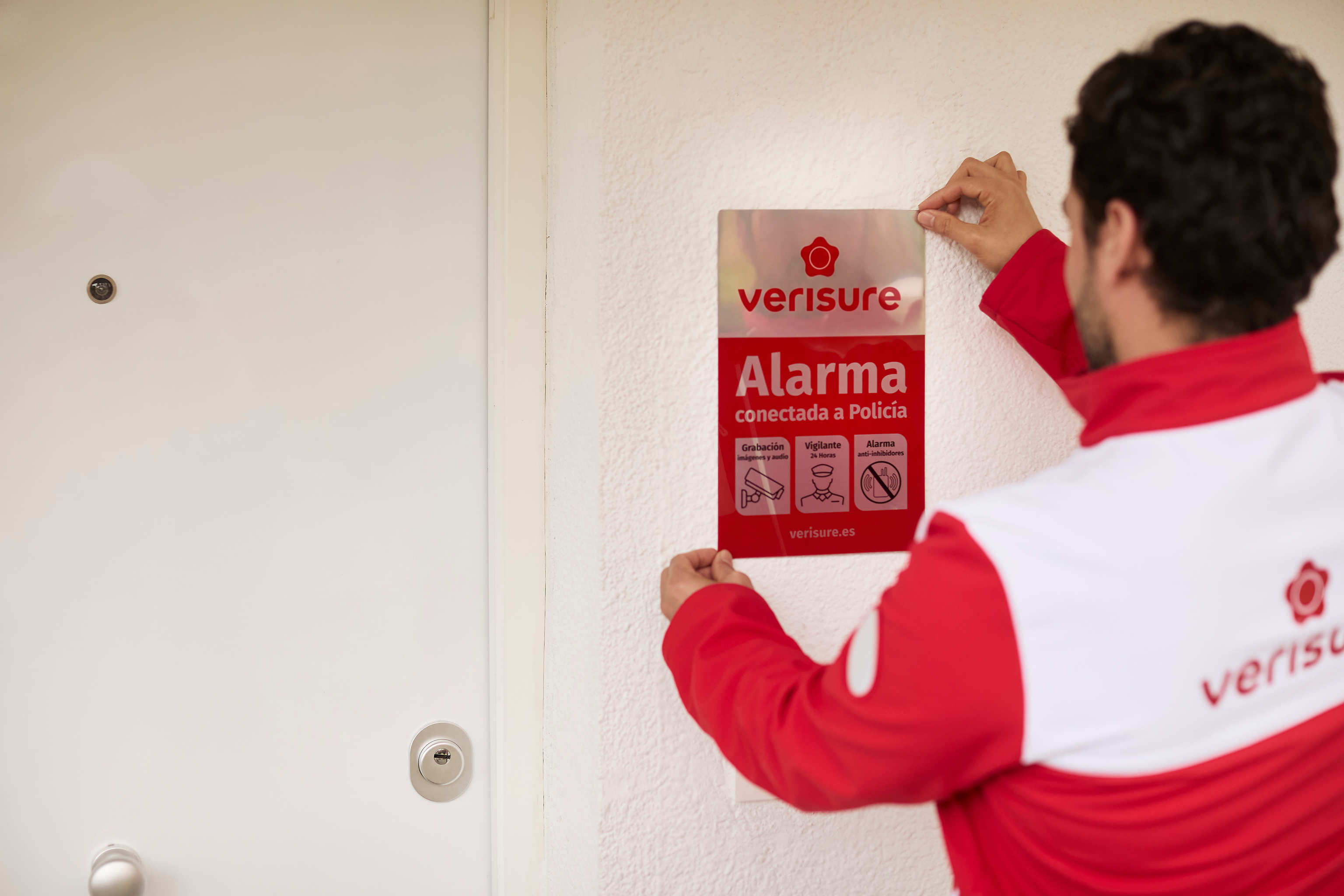 Técnico colocando un cartel desuasorio de Verisure en la puerta de un domicilio.
