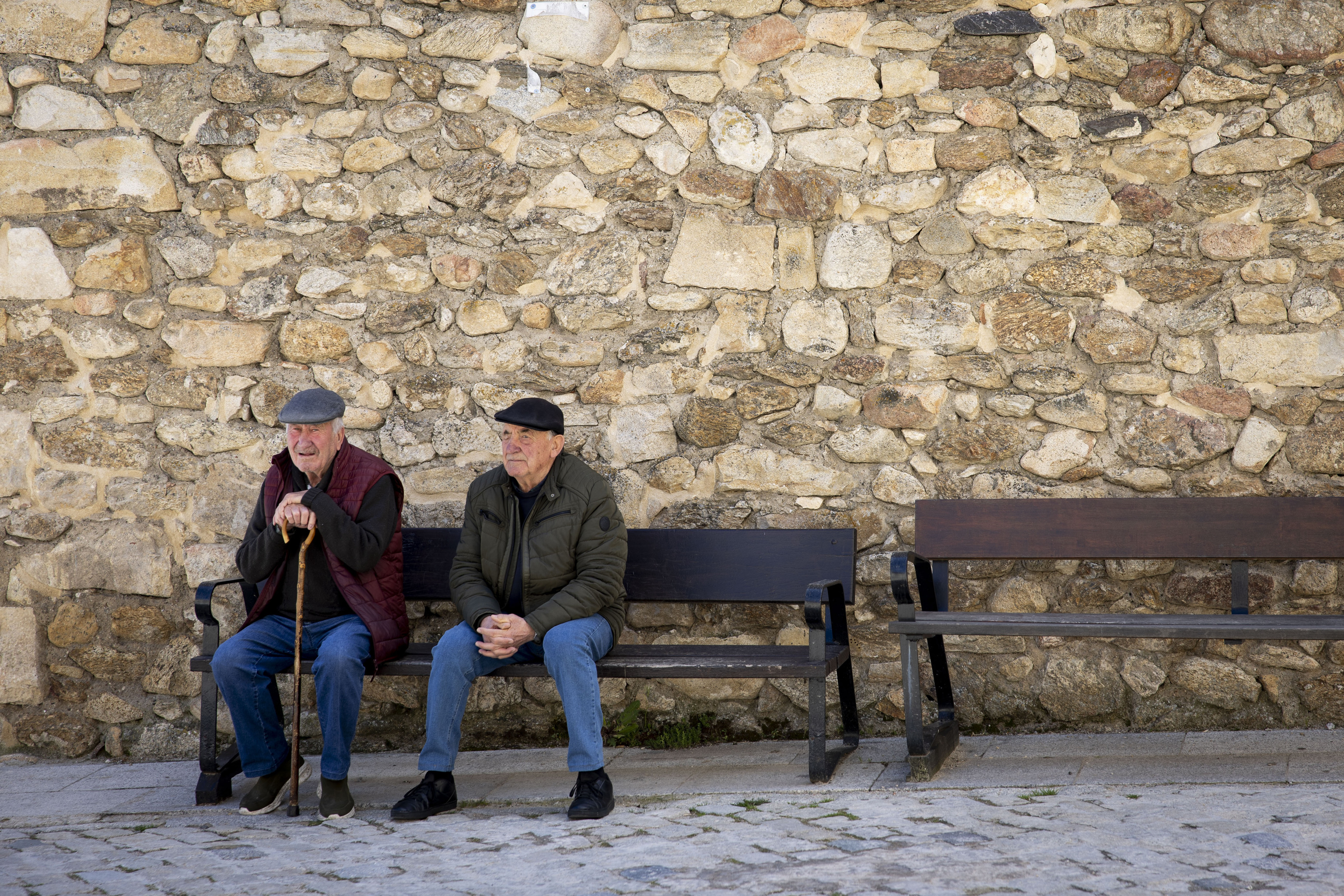 Ventura (a la izquierda, 83 años) en un banco frente a la farmacia. Paqui le prepara un pastillero con su medicación.