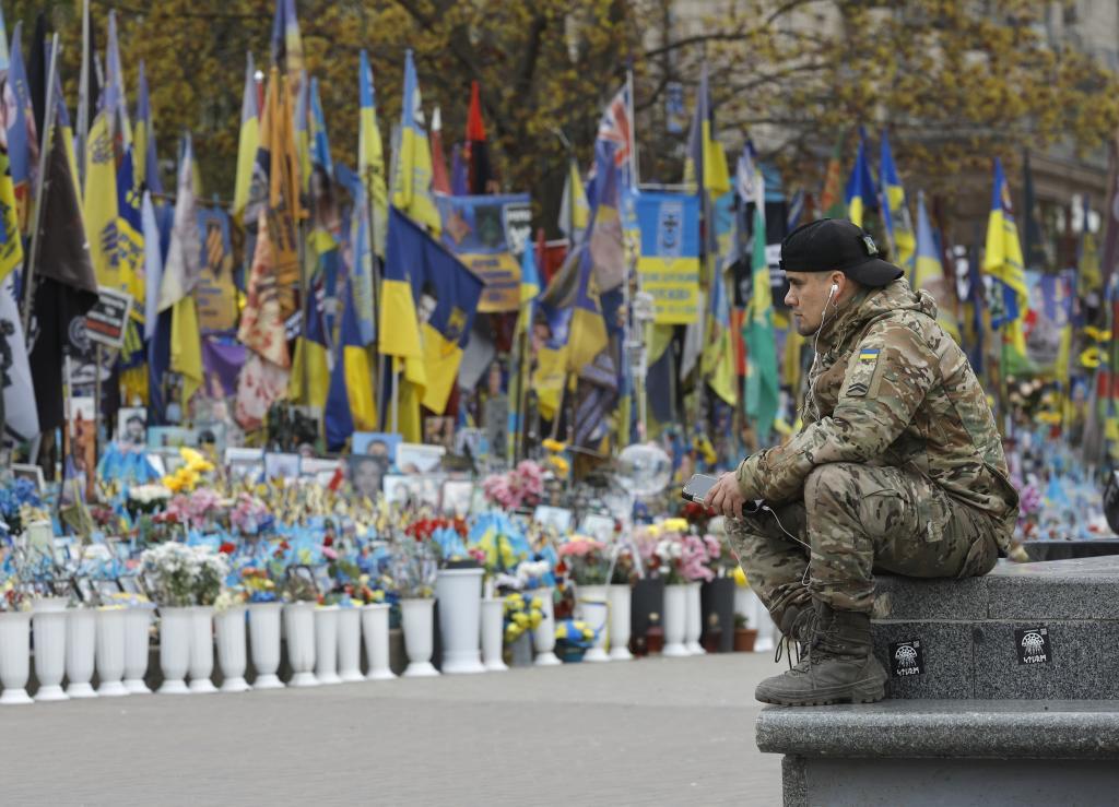 Un hombre con uniforme militar, sentado cerca de un monumento improvisado en Kiev dedicado a los soldados ucranianos caídos.
