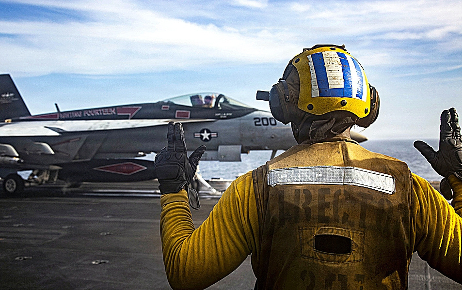Un marinero estadounidense hace señales a un F/A-18E Super Hornet, adscrito al Escuadrón de Cazas de Ataque (VFA) 14, mientras este se prepara para despegar desde la cubierta de vuelo del portaviones Abraham Lincoln.