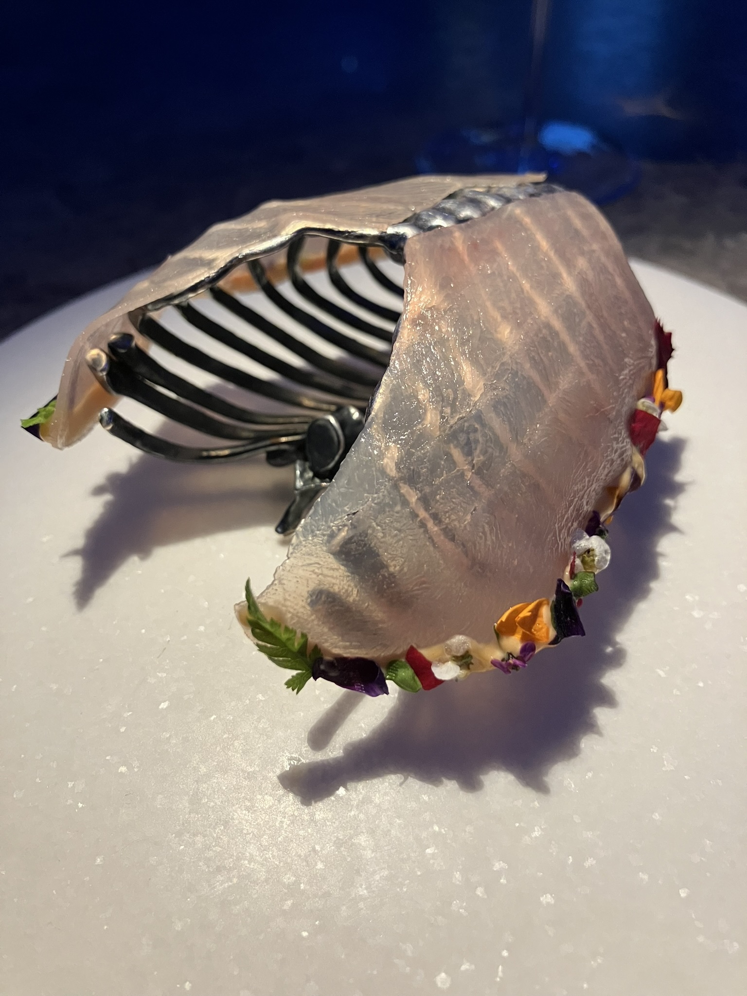 Carne de conejo marinada y adornada con flores, sobre una caja torácica de metal.