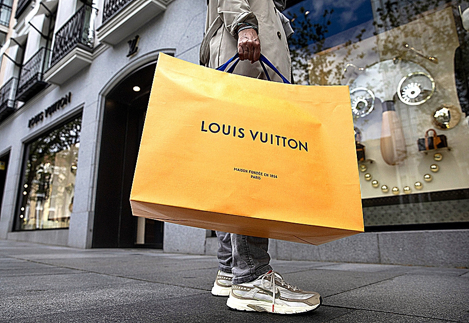 Un cliente sale de una tienda de lujo con una bolsa de Louis Vuitton