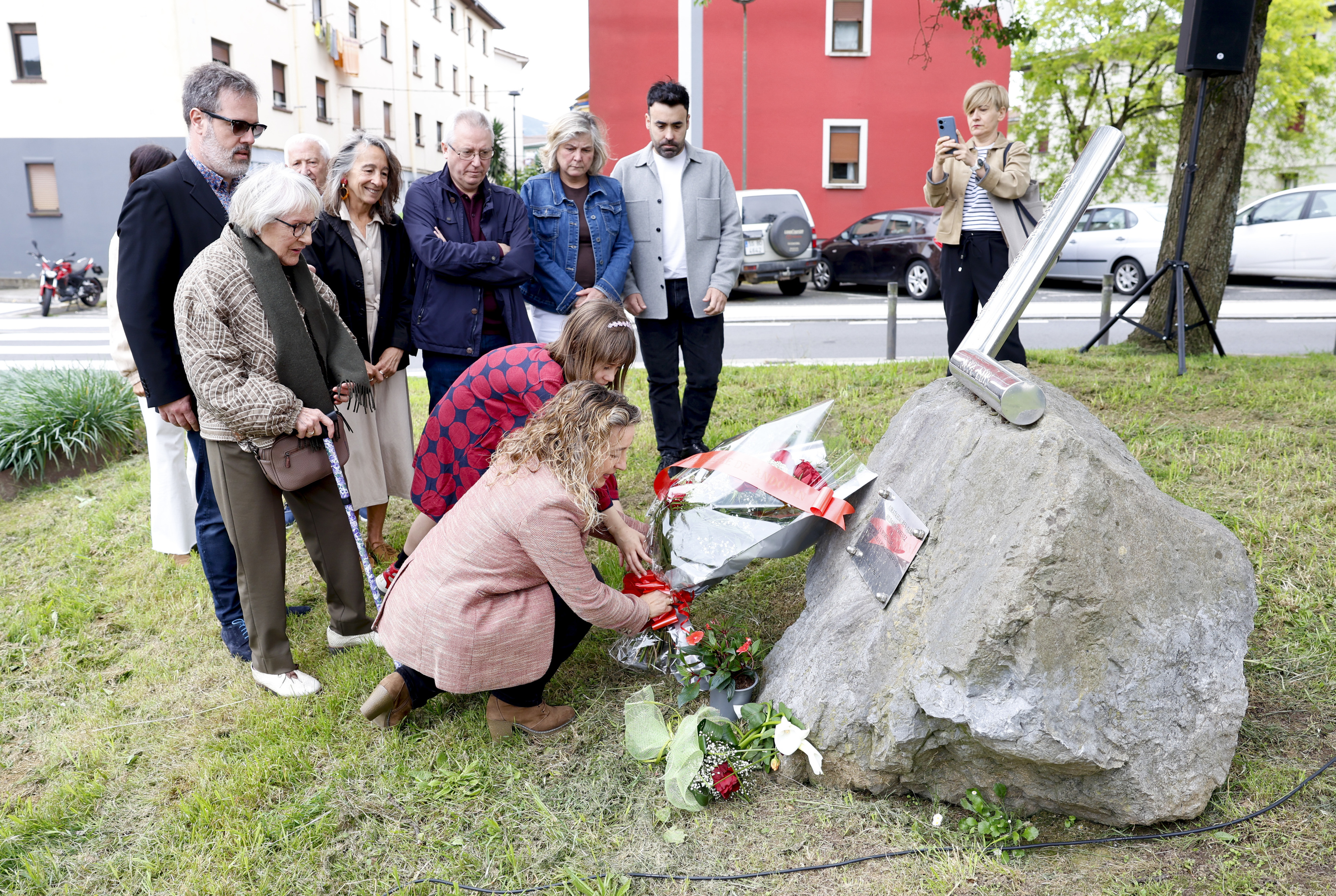 Maider Laínez coloca un ramo de flores junto al monolito en homenaje de José Luis López de Lacalle ante la mirada de Mari Paz Artolazabal y de su hijo Alain.