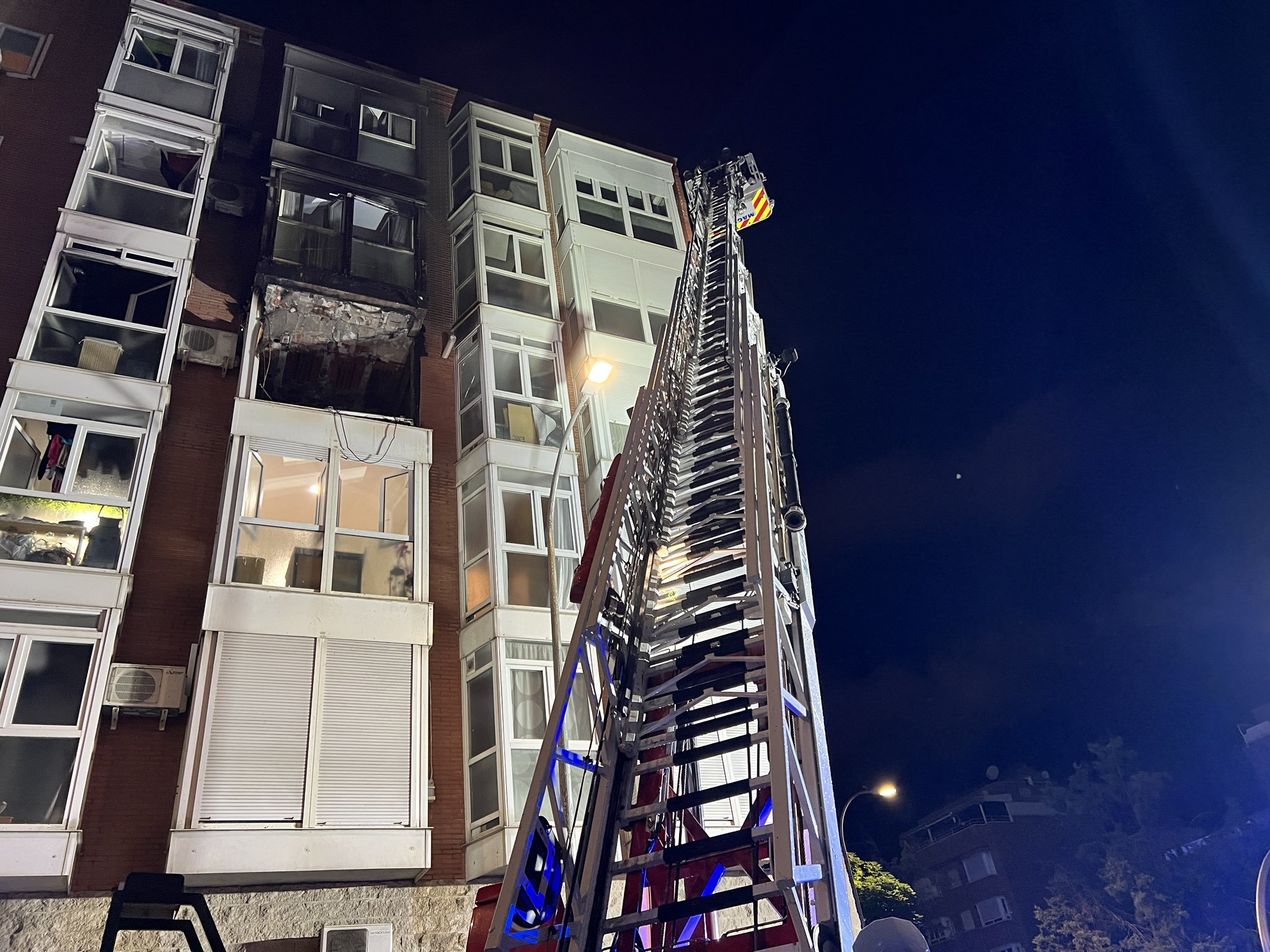 Los bomberos suben por la escalera ante el edificio afectado por las llamas.