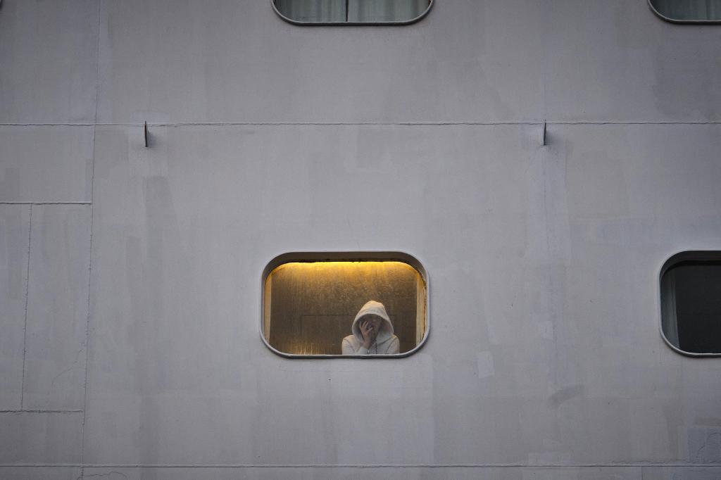 Una persona confinada en el Ambition se asoma a la ventana de su camarote.