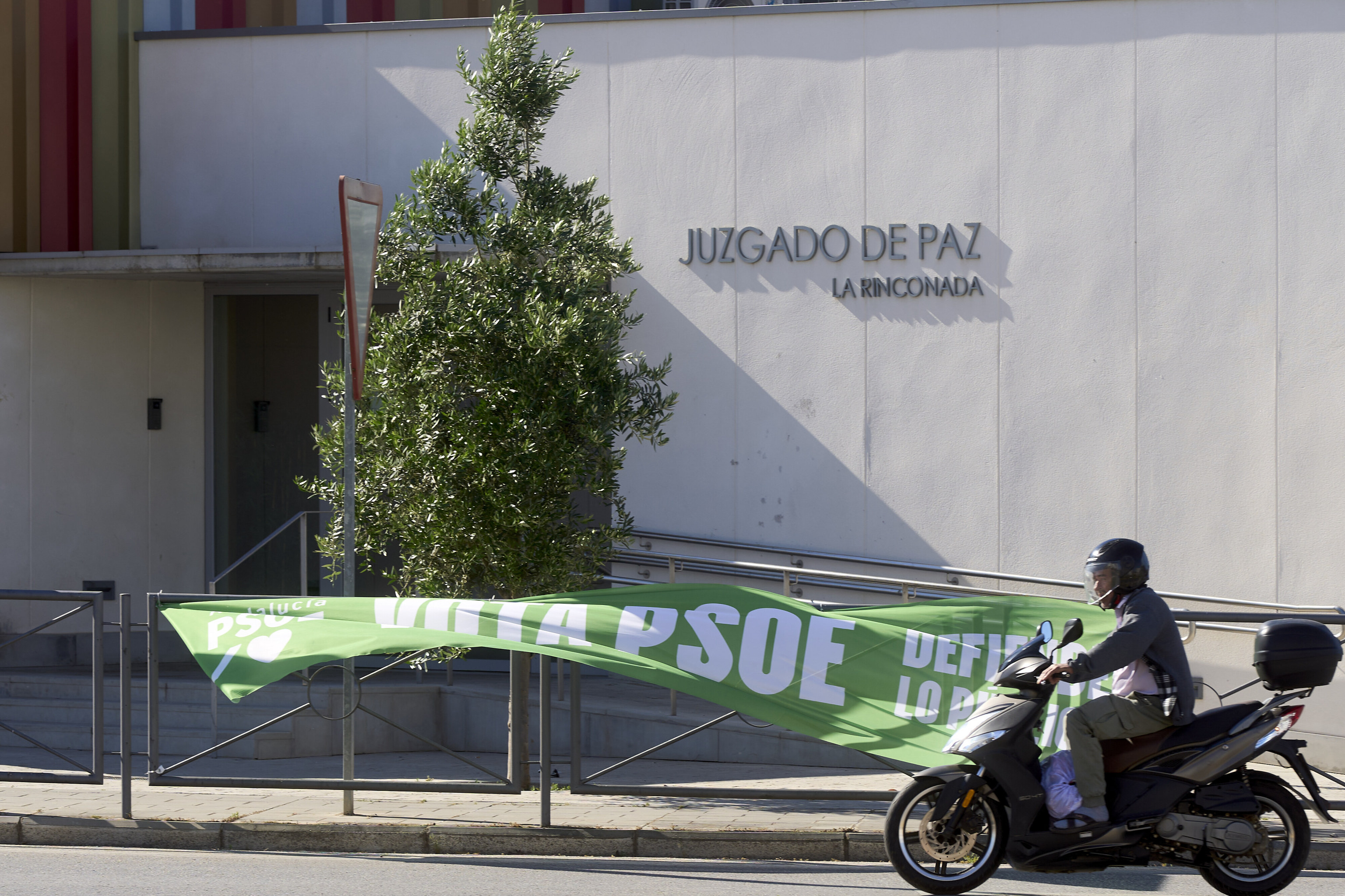 Un motorista pasa junto a un pancarta electoral del PSOE en La Rinconada.