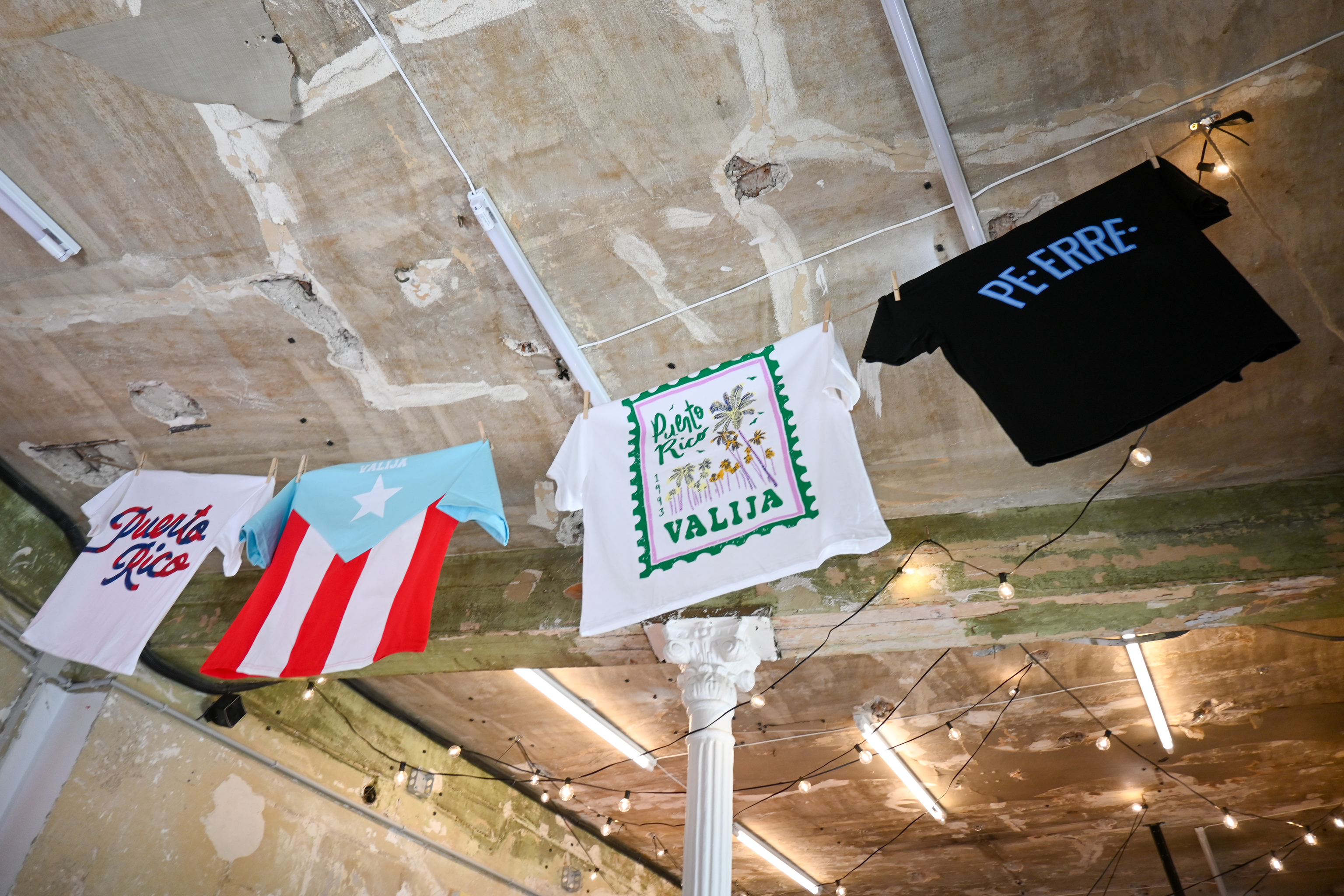 Camisas con diseños boricuas que cuelgan del techo de 'La placita'.