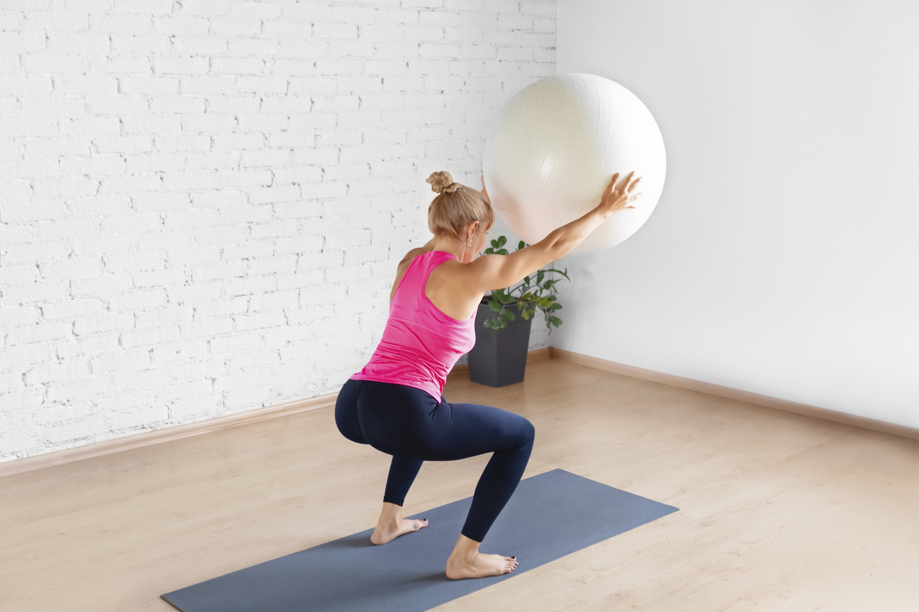 Una mujer hace sentadilla mientras sujeta un balón de fitness.