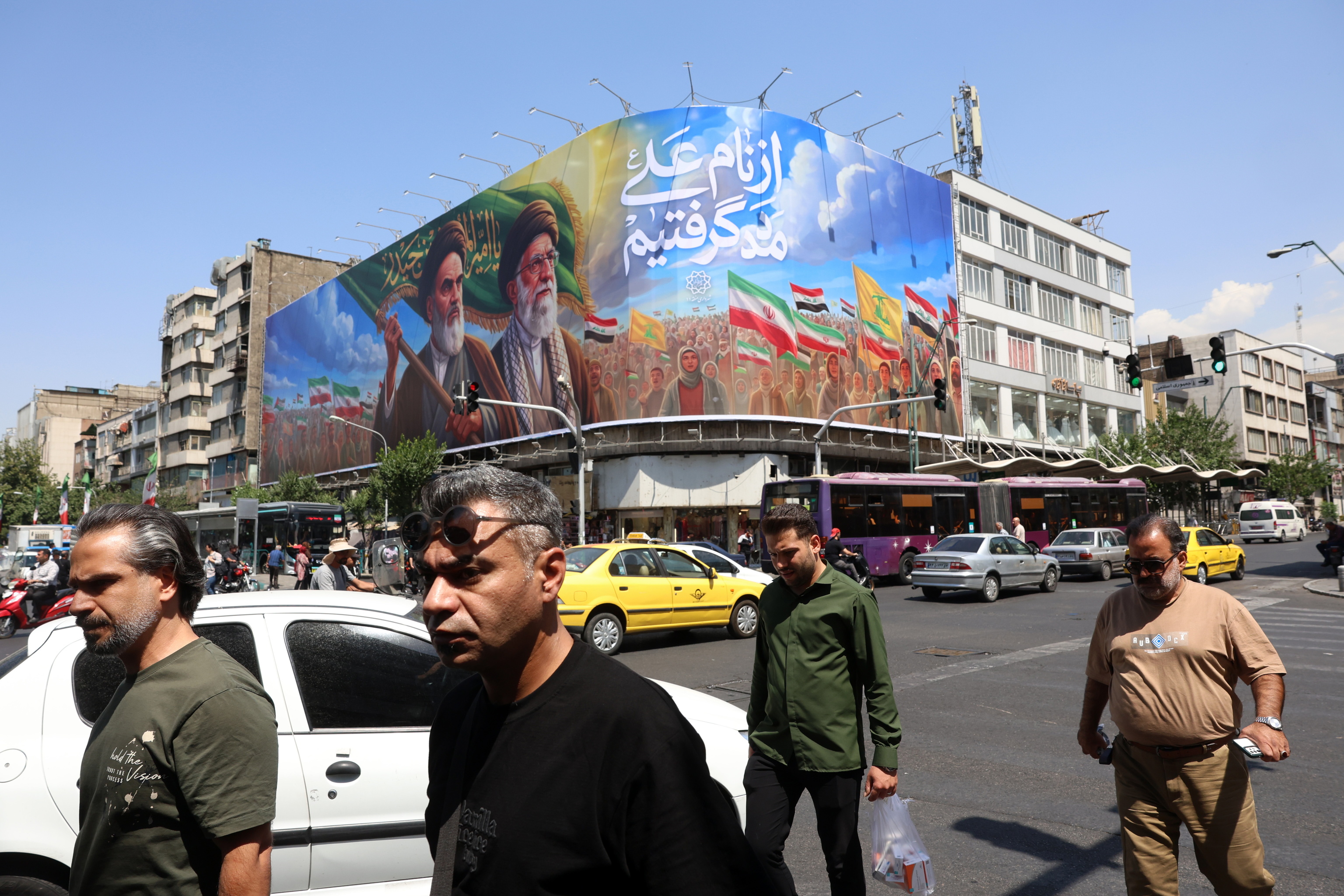 Iraníes pasan cerca de un cartel con los rostros de Jomenei y Jamenei.