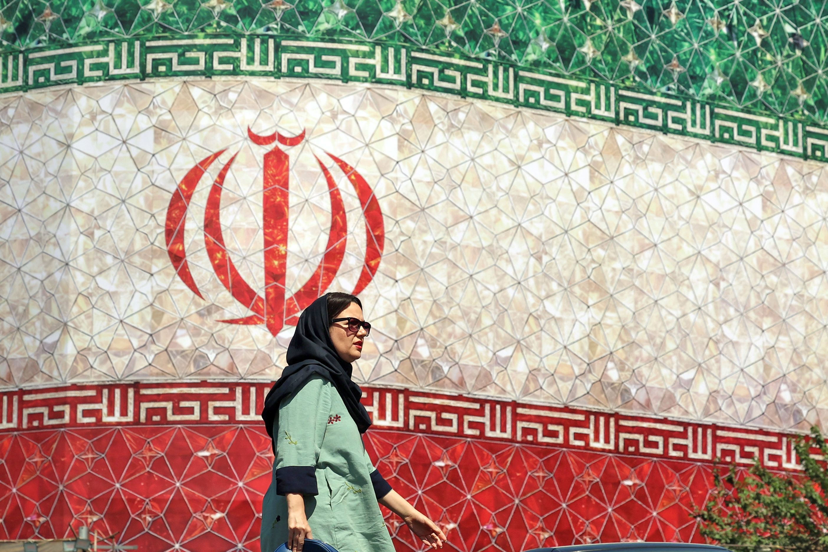 Una mujer pasea por delante de un mural con la bandera de Irán en una calle de Teherán.