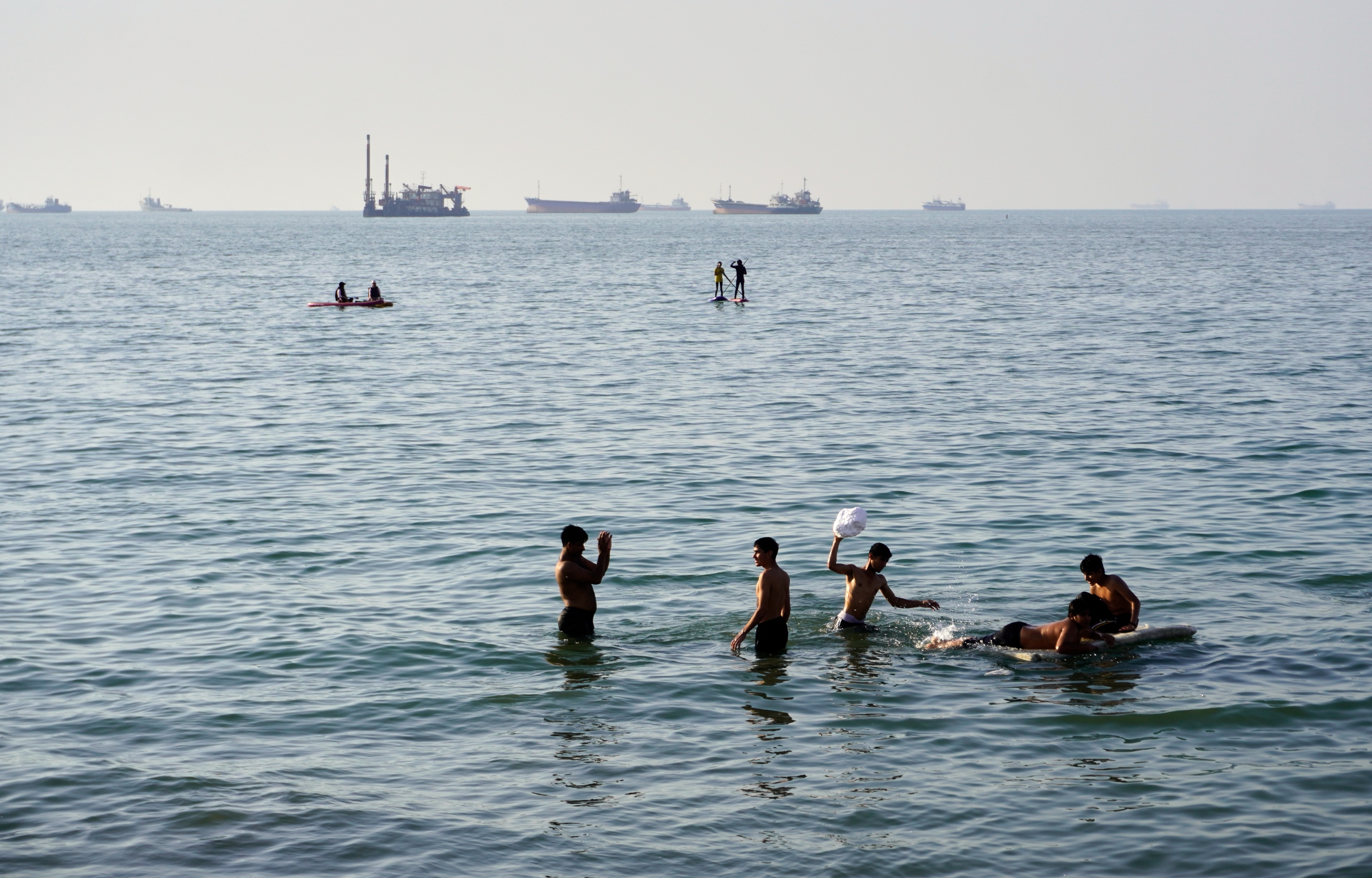 Varios residentes nadan y juegan en las aguas del estrecho de Ormuz; mientras barcos de carga y comerciales permanecen anclados en la distancia frente a Bandar Abbas, Irán, el miércoles 10 de junio de 2026.