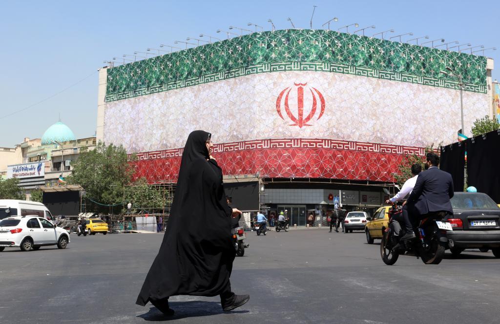 Una mujer iraní con velo pasa junto a una valla publicitaria con la bandera nacional de Irán en la plaza Enqelab de Teherán.