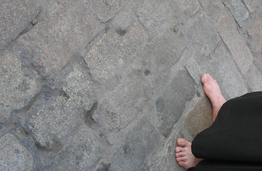 Los pies descalzos de un nazareno pisan el adoquinado de la calle.