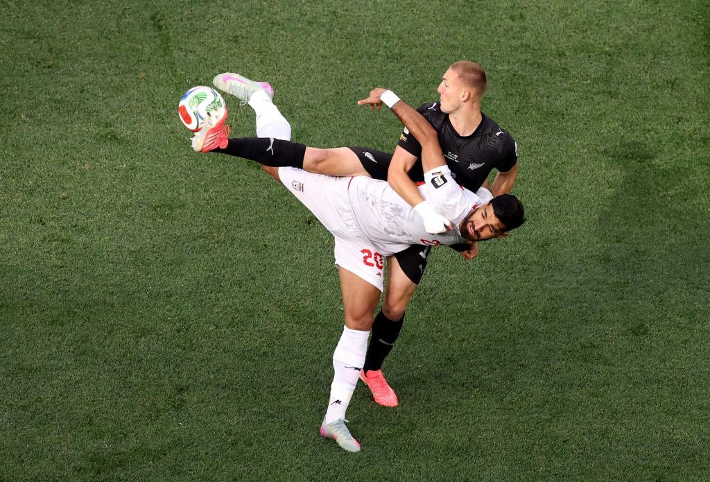El iraní Shahriyar Moghanloo, de blanco, y el neozelandés Finn Surman, de negro, luchan por el balón