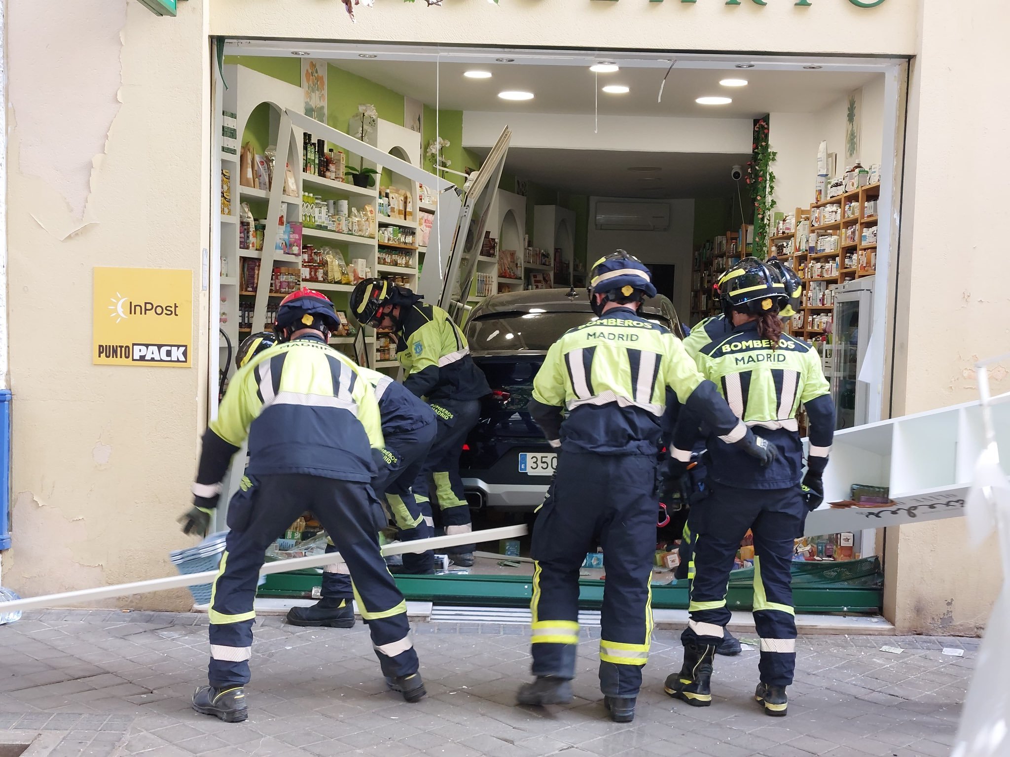 Los bomberos trabajan por sacar el vehículo del comercio, ayer.