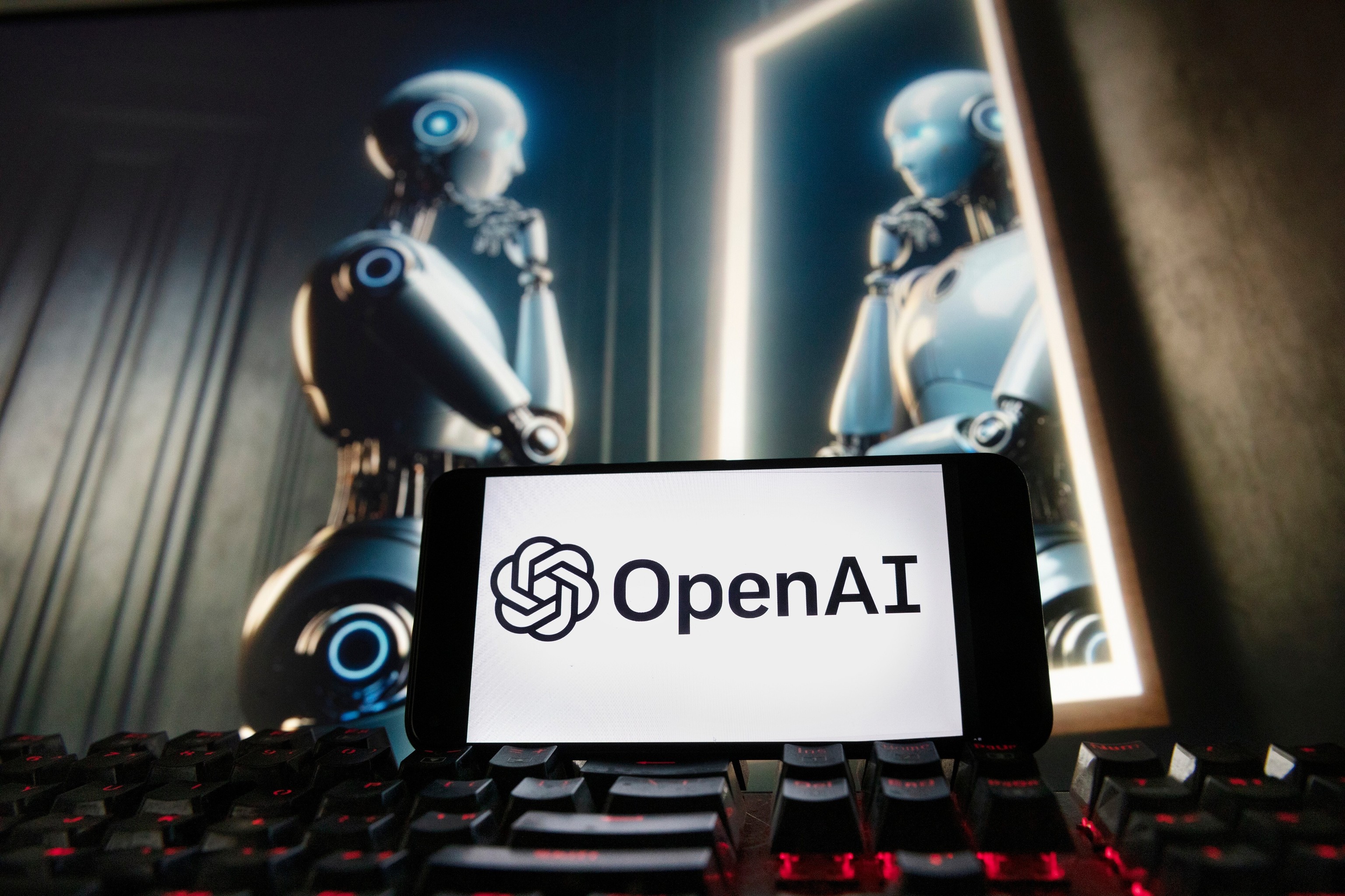 El logotipo de OpenAI aparece en un tel�fono m�vil junto a una imagen en el monitor de una computadora.