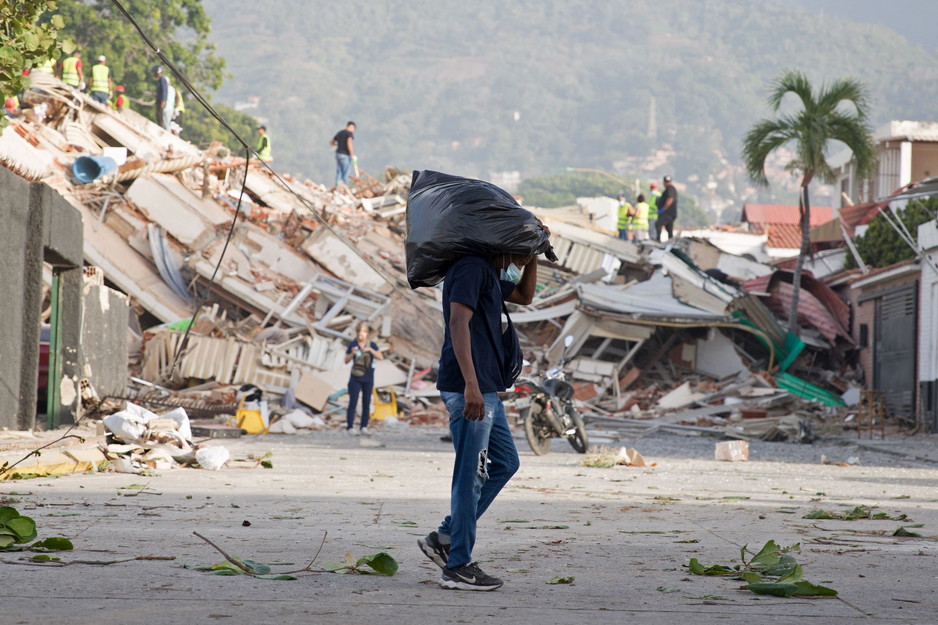 Un hombre lleva una bolsa mientras los voluntarios buscan víctimas entre los escombros de un edificio derrumbado en Caraballeda, en el estado de La Guaira.