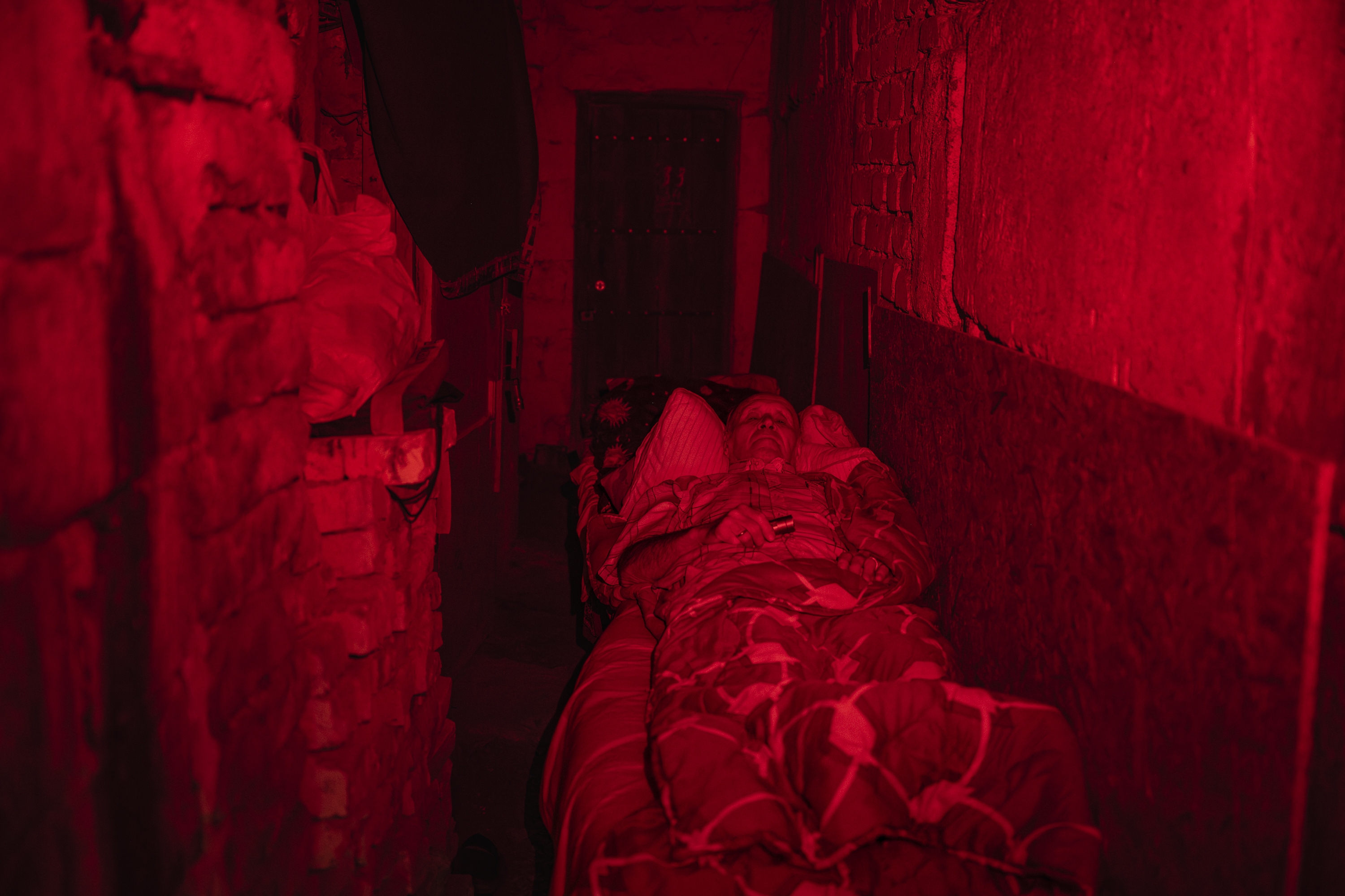 Un anciano yace en la cama dentro de un refugio situado en un sótano de Druzhkivka.