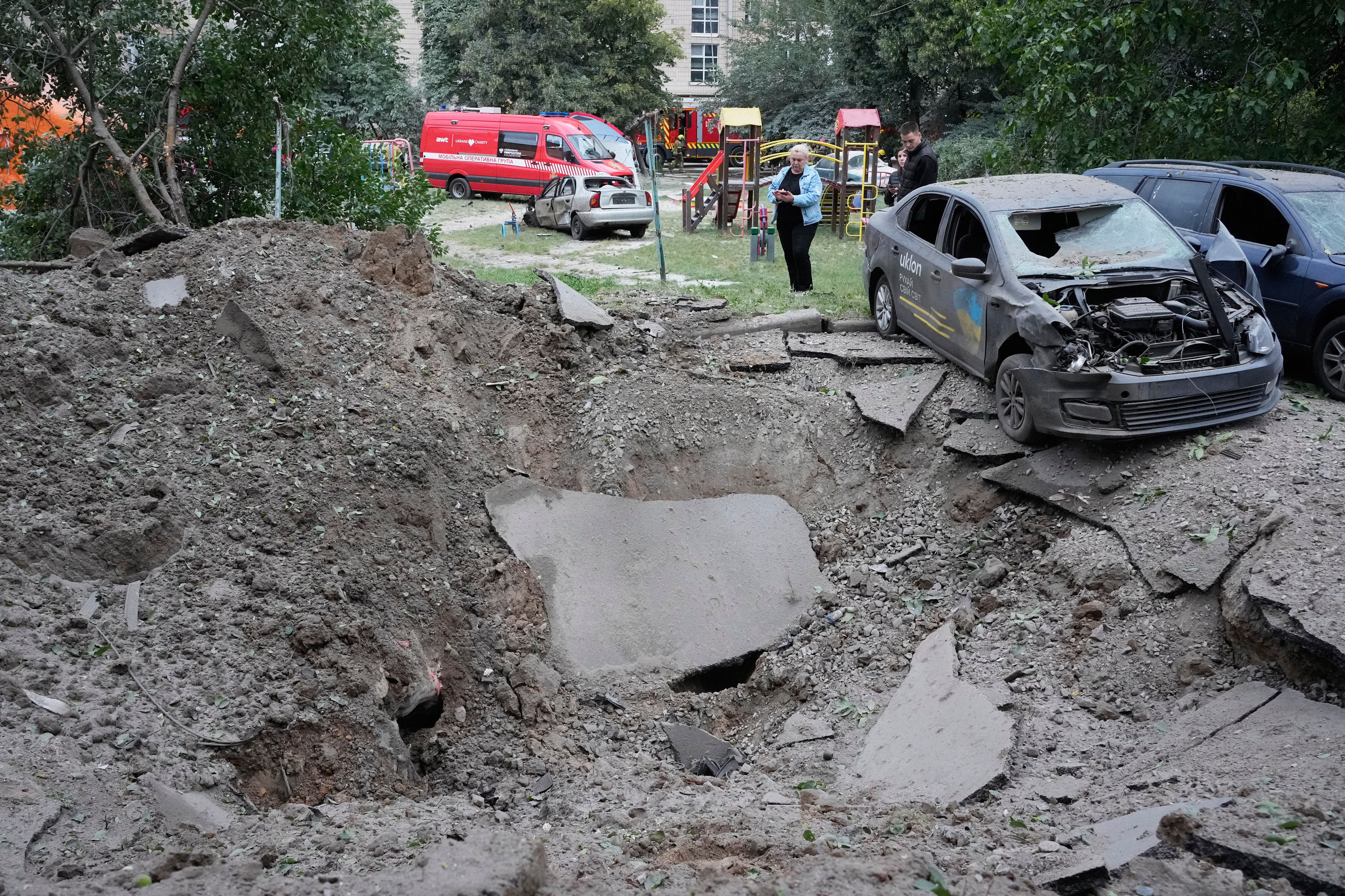 Residentes locales permanecen cerca de un cráter y de automóviles dañados por un ataque con misiles rusos en Kiev