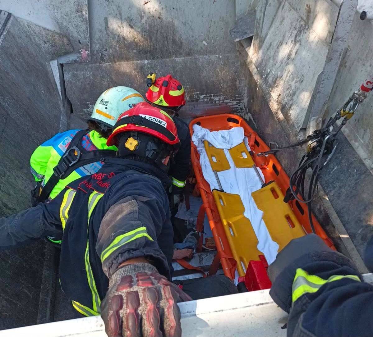 Los bomberos en la caja del camión de reciclajo rescatando a la víctima.