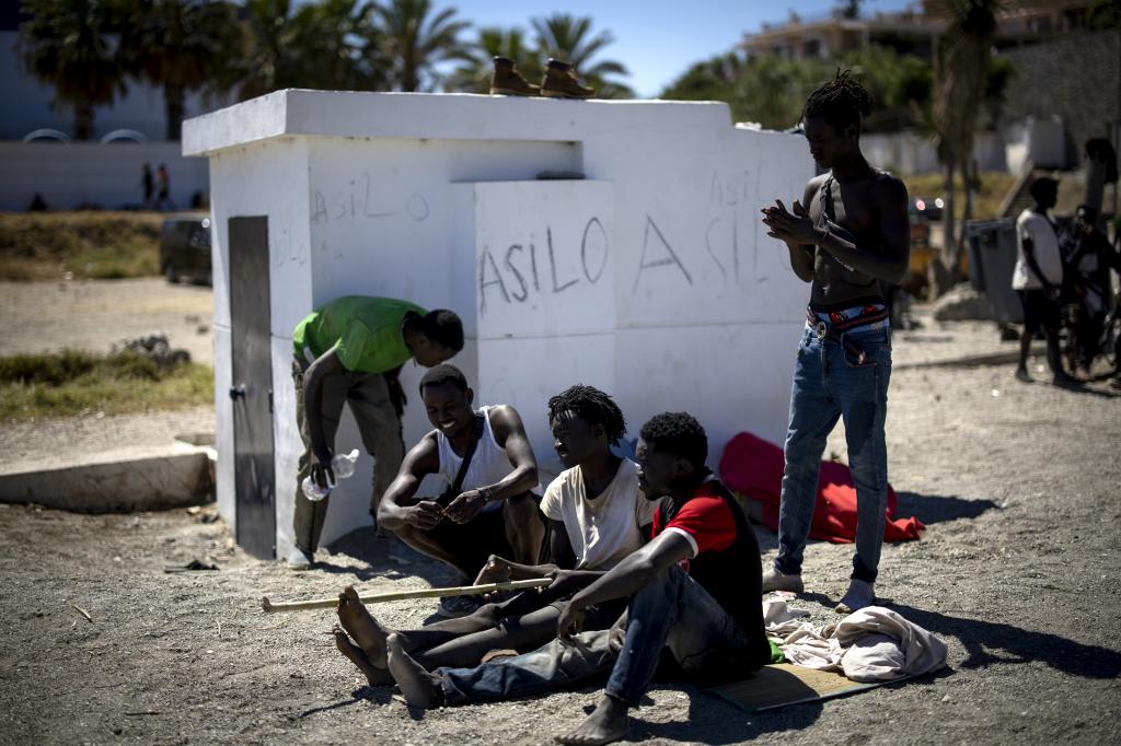 Varios inmigrantes de origen subsahariano, en la playa del Trampolín, junto a una pintada pidiendo asilo.