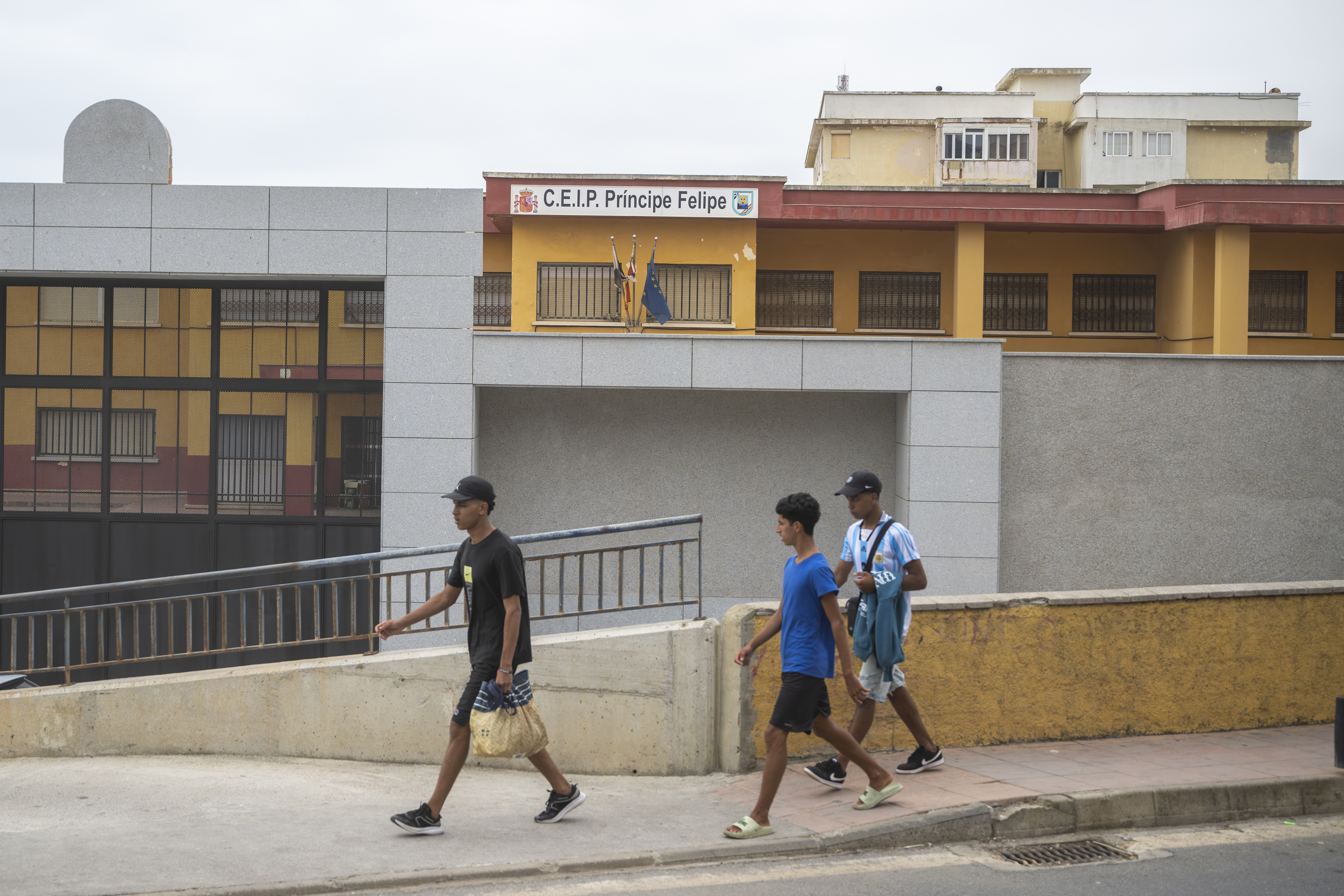 Grupo de jóvenes inmigrantes pasando por delante de la fachada del colegio Príncipe Felipe en Ceuta
