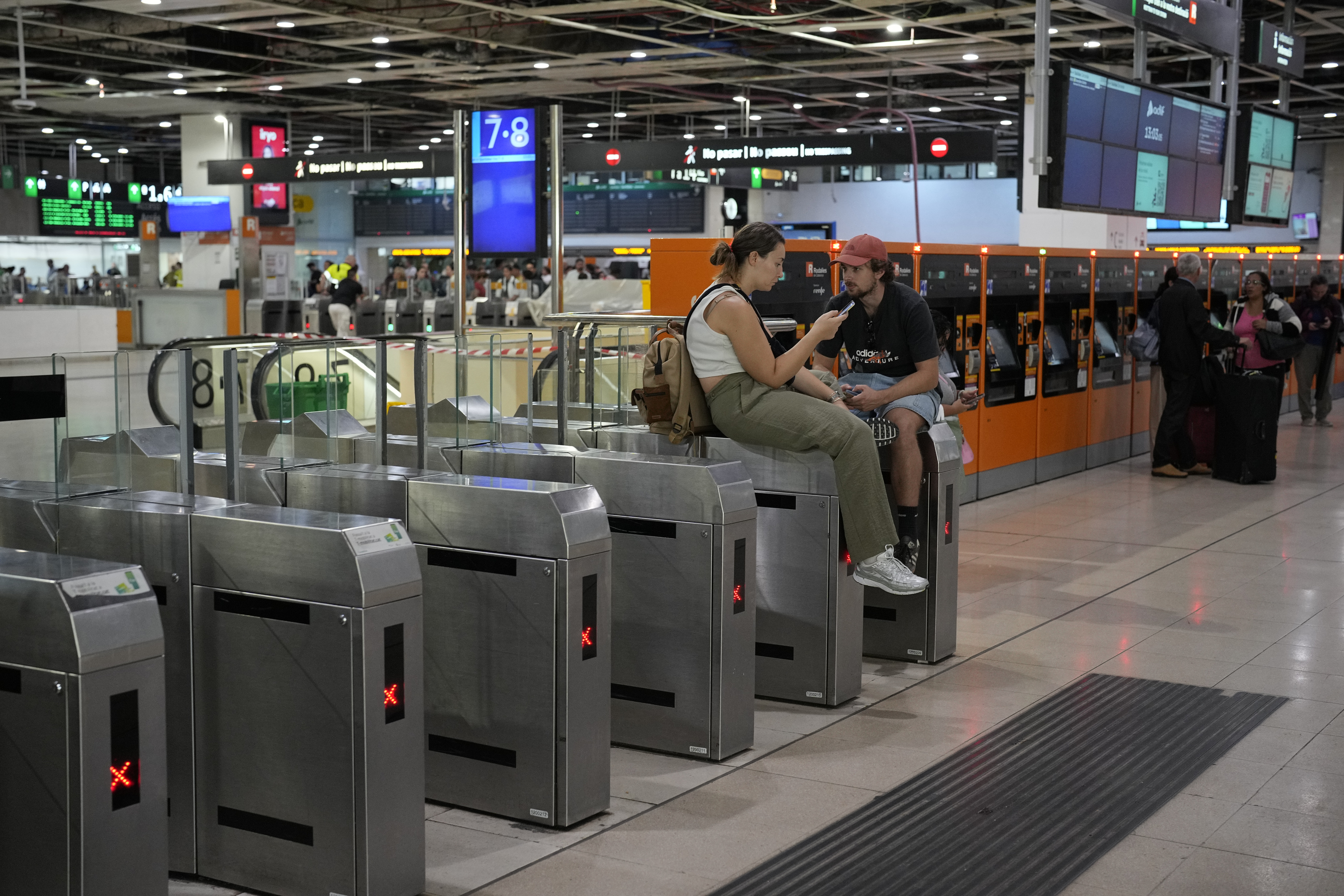 Dos pasajeros sentados encima de los tornos de entrada a una estación de Rodalies.